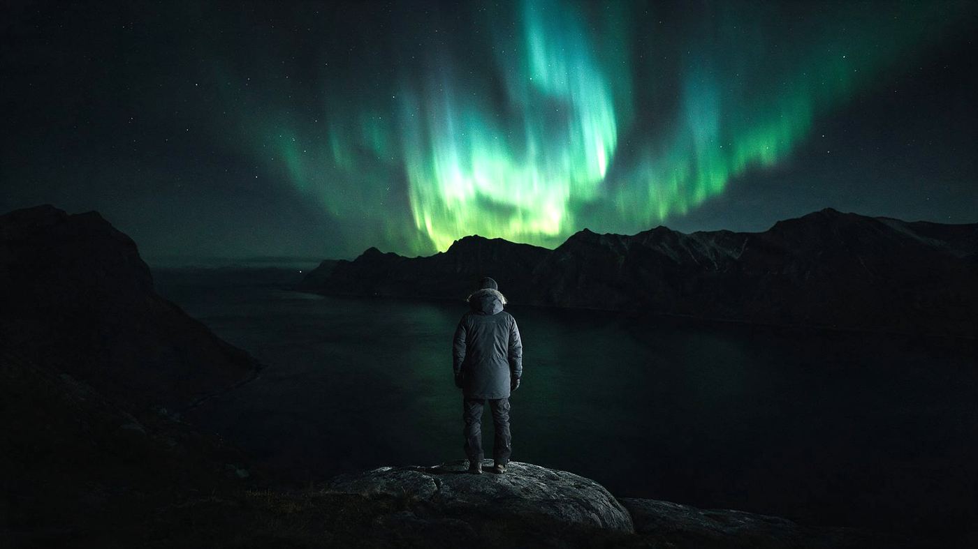A traveler beneath a luminous aurora in the mountains